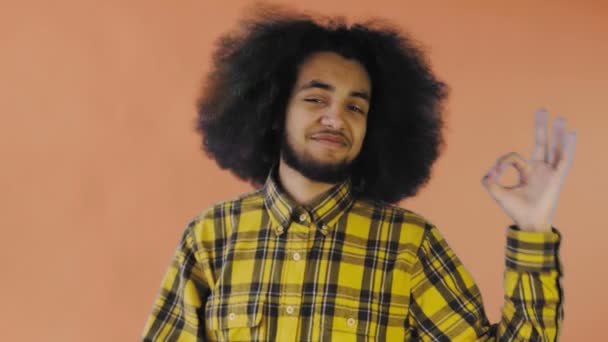 Χαμογελώντας ελκυστική Αφρο-Αμερικανός τύπος δείχνει ok χειρονομία, ενώ στέκεται απομονωμένη πάνω από πορτοκαλί φόντο. Έννοια των συναισθημάτων — Αρχείο Βίντεο