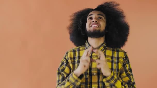 Retrato de un chico afroamericano rezando manteniendo los dedos cruzados y gritando dios por favor sobre fondo naranja. Concepto de emociones — Vídeo de stock