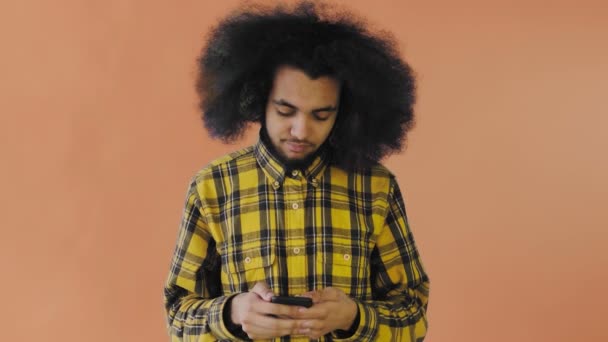 Mladý pohledný africký Američan používající telefon na oranžovém pozadí. Pojetí emocí — Stock video