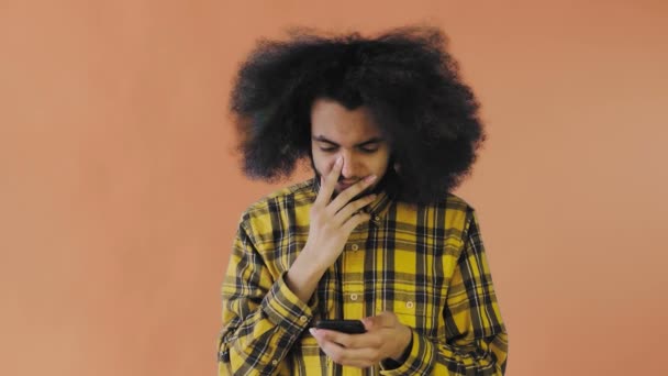 Giovane uomo afro-americano triste utilizzando il telefono e ricevendo cattive notizie su sfondo arancione. Concetto di emozioni — Video Stock