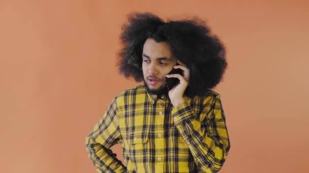 Felice attraente giovane afro-americano che parla sul cellulare su sfondo arancione. Concetto di emozioni — Video Stock