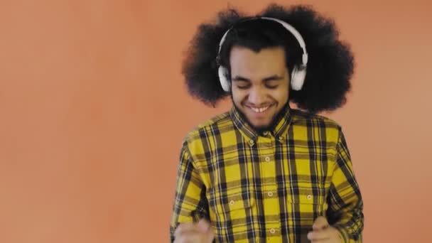 Θετικός Αφροαμερικάνος ακούει μουσική με τα ακουστικά του στο πορτοκαλί φόντο. Έννοια των συναισθημάτων — Αρχείο Βίντεο