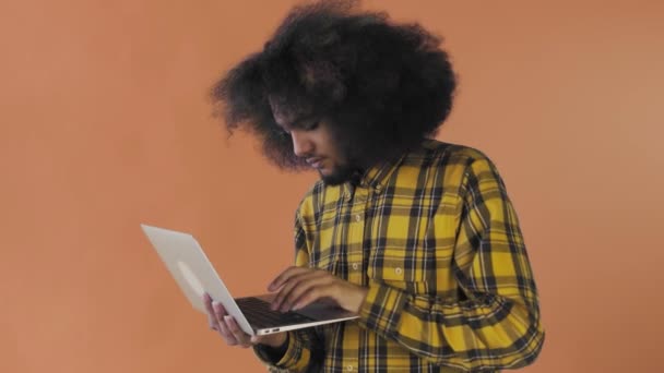 Щасливий афроамериканець, який користується ноутбуком на помаранчевому тлі. Концепція емоцій — стокове відео