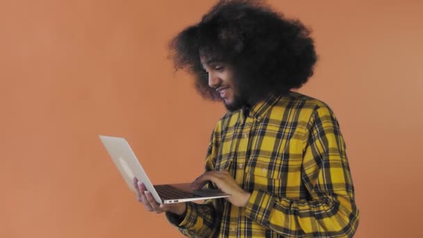 Vrolijke Afro-Amerikaanse man met behulp van laptop, glimlachend en weg te gaan op Orange achtergrond. Concept van emoties — Stockvideo