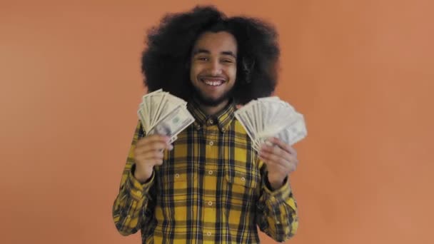 Jovem afro-americano segurando dinheiro em dinheiro em fundo laranja . — Vídeo de Stock