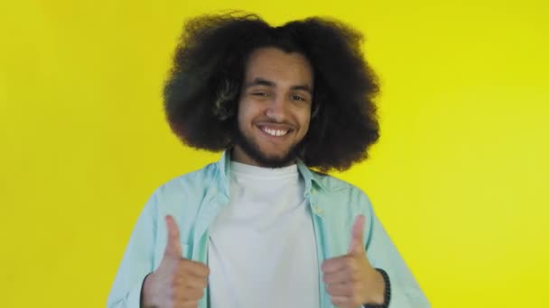 Afro amerikai férfi mosolyog, miközben felemeli a hüvelykujját a sárga háttérben. Az érzelmek fogalma — Stock videók