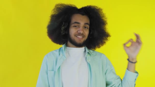 黄色の背景の上に隔離された立っている間、 ［OK］をジェスチャーを示す魅力的なアフリカ系アメリカ人の男を笑顔。感情の概念 — ストック動画