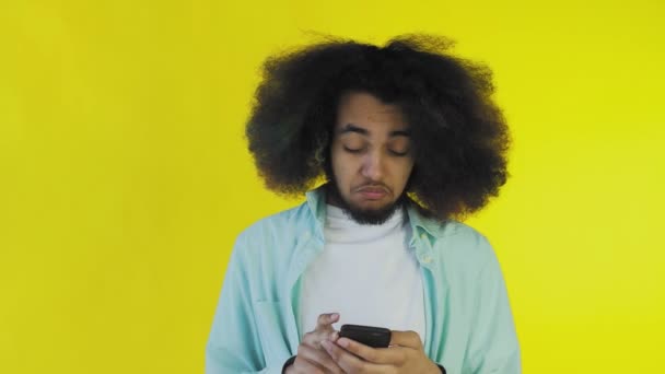 Giovane afro-americano che usa il telefono e riceve buone notizie su sfondo giallo. Concetto di emozioni — Video Stock