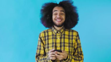 Genç mutlu Afrikalı işadamı telefonu kullanıyor ve Mavi arka planda iyi haberler alıyor. Duyguların kavramı