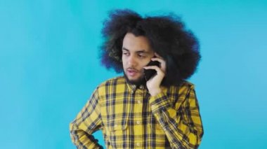 Mavi arka planda cep telefonuyla konuşan mutlu Afro-Amerikalı adam. Duyguların kavramı