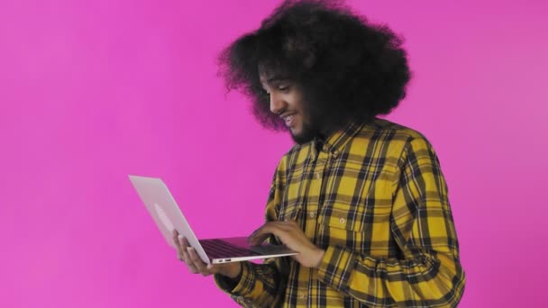 Felice uomo afroamericano utilizzando il computer portatile, sorridente e andare via su sfondo viola. Concetto di emozioni — Video Stock