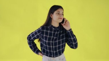 Sarı arka planda tek başına duran genç bir kadın telefonla konuşuyor.