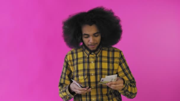 Joven afroamericano contando dinero en efectivo sobre fondo púrpura . — Vídeo de stock