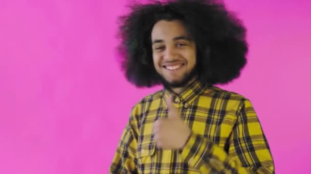 Młody, szczęśliwy afro-Amerykanin uśmiecha się, podnosząc kciuki na fioletowym tle. Pojęcie emocji — Wideo stockowe