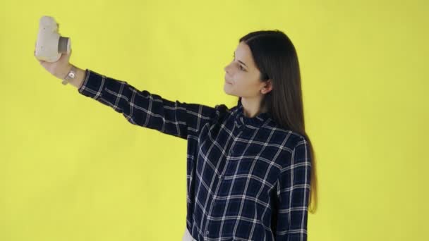 Hermosa chica tomando selfie en la cámara de fotos retro sobre fondo amarillo en el estudio — Vídeo de stock