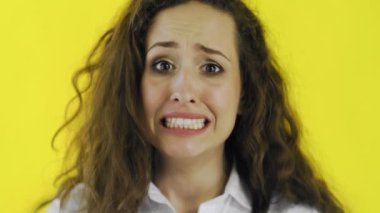 Utanmış bir kadın, sarı arka planda izole bir şekilde dikilip kameraya bakıyor.