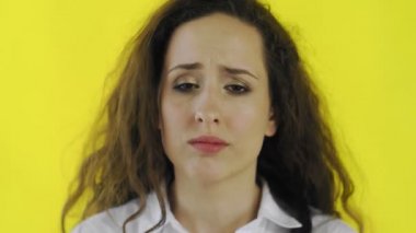 Üzücü, düşünceli, tişörtlü güzel bir kadın. Stüdyoda sarı arka planda duruyor..