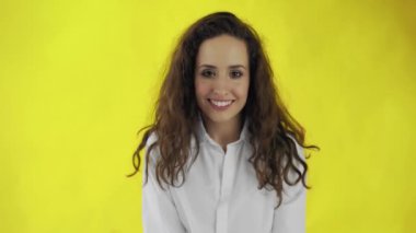 Güzel bir kadın göz kırpıyor ve sarı arka planla stüdyoda ağzını açıyor..