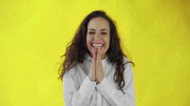 Güzel, esmer, uzun saçlı bir kadının portresi. Sarı arka planda elleri olan mutlu bir şekilde ağzını kapatıyor.