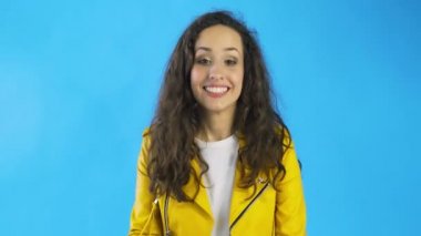 Genç, neşeli bir kadın gülüyor. Stüdyoda elleri ve mavi arka planı ile ağzını kapatıyor..