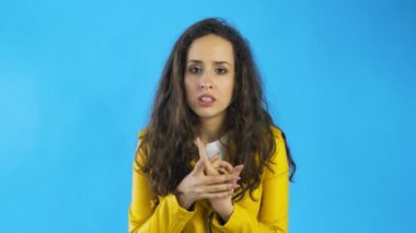 Gergin, güzel, beyaz, uzun kahverengi saçlı, elleri ovuşturan bir kadın. Stüdyoda mavi arka planda tırnaklarını yiyor..