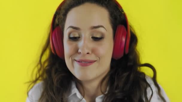 黄色の背景を持つスタジオで赤いヘッドフォンで音楽を聴く女性. — ストック動画