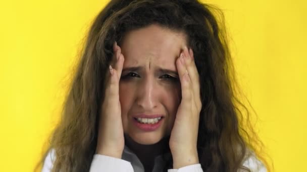 Beautiful girl is suffering from a migraine standing on a yellow background, slow motion — Stock Video