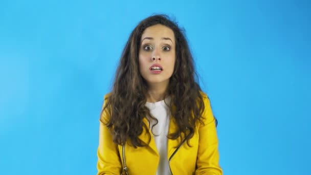 Portrét překvapené ženy s kudrnatými vlasy vyjadřující neočekávanost nebo šok v ateliéru s modrým pozadím. — Stock video