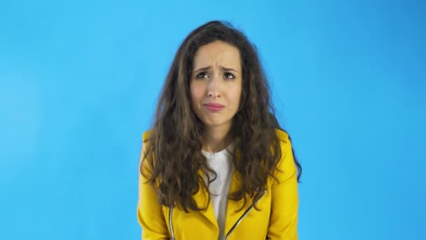 Mujer joven confusa en chaqueta amarilla en Studio con fondo azul . — Vídeos de Stock