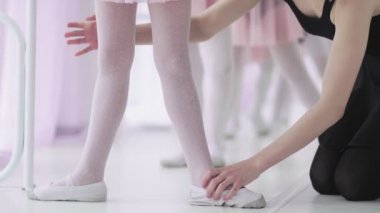 Beyaz çoraplı ve bale ayakkabılı tanınmayan küçük kızların ayaklarını kapat. Bale hocaları onları düzeltiyor.