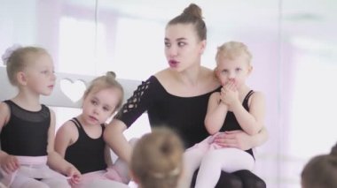 Genç bale öğretmeni, bale okulunda siyah taytlı küçük kızlarla oturuyor ve onlarla iletişim kuruyor.