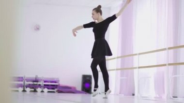 Siyah sırt çantalı profesyonel bir balerin büyük bir eğitim salonunda dans ediyor.