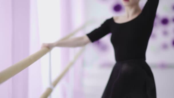 Молода тонка балерина в чорній сукні танцює або розтягується біля великого вікна . — стокове відео