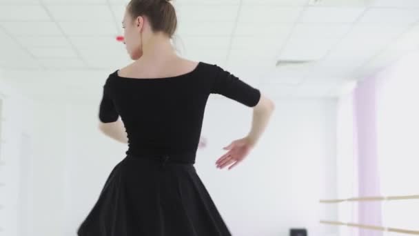 A professional ballerina in a black pack dances in a large training hall — Stock Video