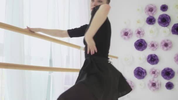 Geautiful ballerina dressed in black tutu dancing near a big window. — Stock Video