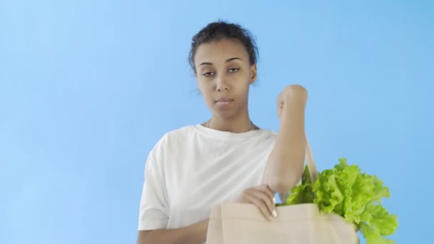Mavi arka planda sebzeli çanta taşıyan kadın. — Stok video