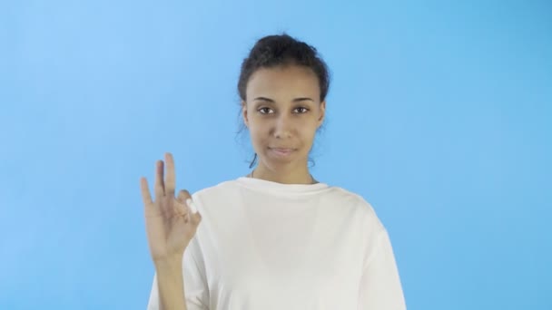CuteAfro-American Girl δείχνει εντάξει με δύο αντίχειρες και χαμογελώντας σε μπλε φόντο στο στούντιο — Αρχείο Βίντεο