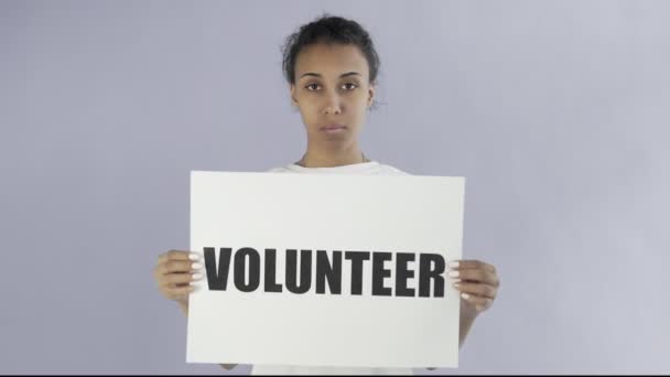 Афроамериканская девушка-активистка с плакатом волонтера на сером фоне — стоковое видео