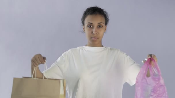 Афро-американська дівчина-активістка робить вибір між папером і пластиковим пакетом на сірому фоні — стокове відео