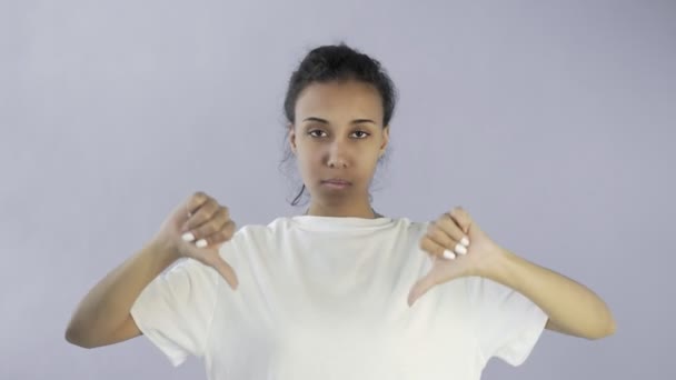 Beautiful young girl in a white T-shirt shows thumb down with both hands on grey background — Stock Video