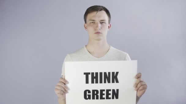 Mladý muž aktivista s think green plakát na šedém pozadí — Stock video