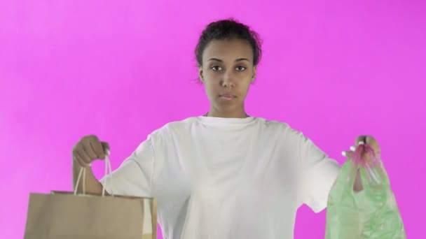Афро-американская девушка-активистка делает выбор между бумагой и пластиковым пакетом на розовом фоне — стоковое видео