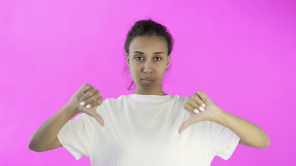 Menina bonita em uma camiseta branca mostra polegar para baixo com ambas as mãos no fundo rosa — Vídeo de Stock