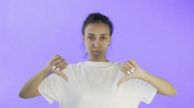 Beyaz tişörtlü güzel bir genç kız iki eli Violet 'in arka planında baş parmağını aşağı gösteriyor.