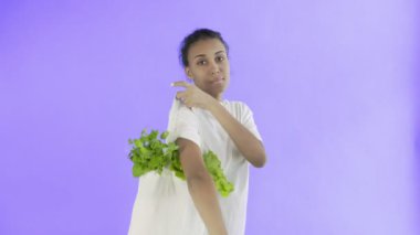 Violet 'in arka planında sebzeli çanta taşıyan kadın.