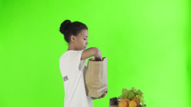 Szczęśliwa kobieta załadować torbę papierową z organicznych zdrowych warzyw i owoców na tle klucza chroma — Wideo stockowe