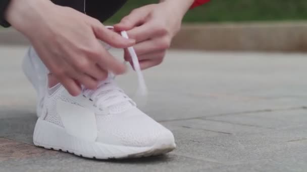 A női sportoló cipőfűzőt, fehér tornacipőt, fehér zoknit köt, sportruhában fut az utcán.. — Stock videók