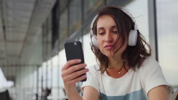 ヘッドフォンで音楽を聞いて、スマートフォンでチャットの若い女性 — ストック動画