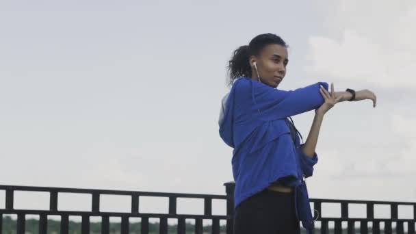 Afroamerykanka biegacz kobieta wyciąga ramiona, aby przygotować się do biegania na ulicy, Zdrowa młoda piękna kobieta ćwiczenia w pobliżu rzeki. — Wideo stockowe