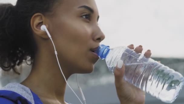 Afrikansk amerikansk tonåring flicka dricker kallt vatten efter att ha kört i parken i friska luften under solig dag — Stockvideo